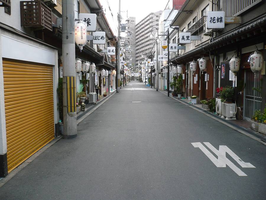 An empty morning street in Tobita Shinchi, Osaka, lined on both sides with low wooden buildings, white paper lanterns and hanging name signboards